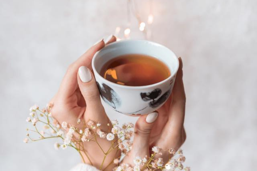 brown-house-and-tea-z-pasji-do-herbat-kraftowych-filizanka-herbaty-w-dloniach-kobiety-delikatne-biale-kwiaty-oplataja-rece