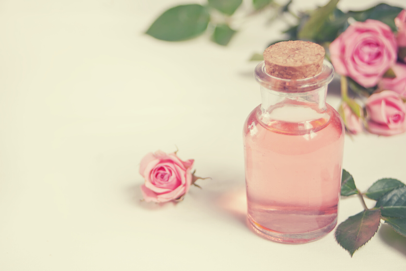 hydrolat-rozany-wlasciwosci-delikatnie-rowa-woda-z-platkow-roz-w-szklanej-przezroczystej-buteleczce-paki-jasnorozowej-rozy-na-jasnym-tle
