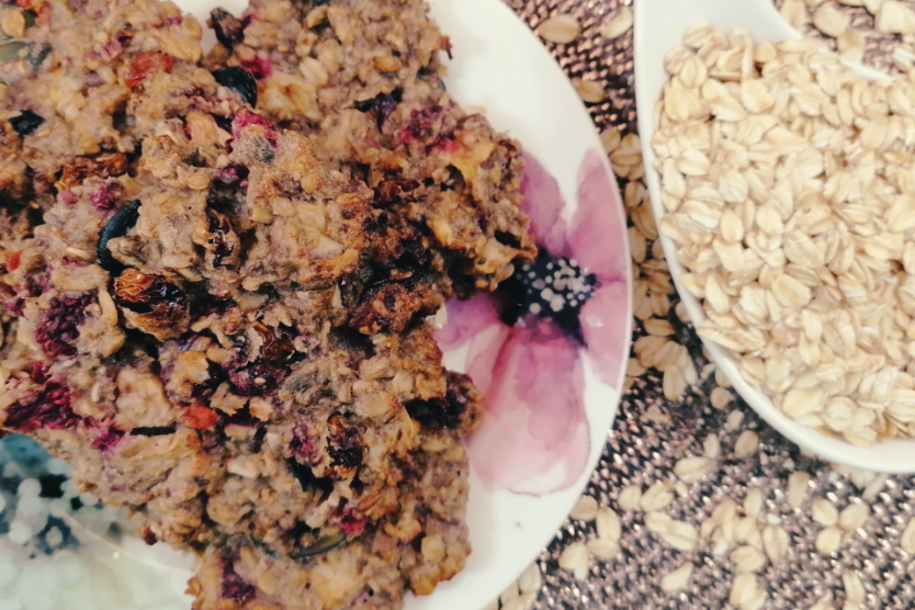 ciasteczka-owsiane-z-bananami-zurawina-pestkami-dyni-slonecznikiem-jablkami-malinami-na-jasnym-talerzu-z-kwietnym-motywem-platki-owsiane-w-bialej-ceramicznej-lyzce-1200x64