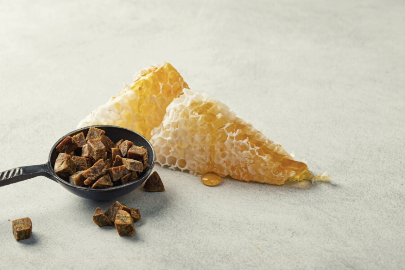 co-to-jest-propolis-i-jak-go-stosowac-propolis-na-metalowej-lyzce-plaster-miodu-jasnoszare-tlo