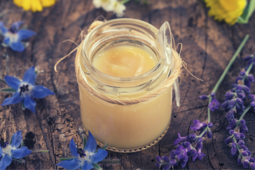 mleczko-pszczele-w-szklanym-sloiku-na-drewnianym-stole-w-tle-kolorowe-polne-kwiaty