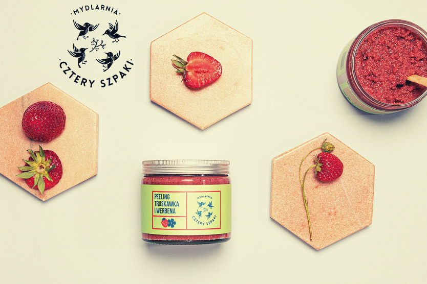 mydlarnia-4-szpaki-ekologiczne-kosmetyki-ktore-urzekaja-peeling-truskawka-werbena-na-jasnym-tle-logo-4-szpaki-owoce-truskawki-na-heksagonalnych-plytkach