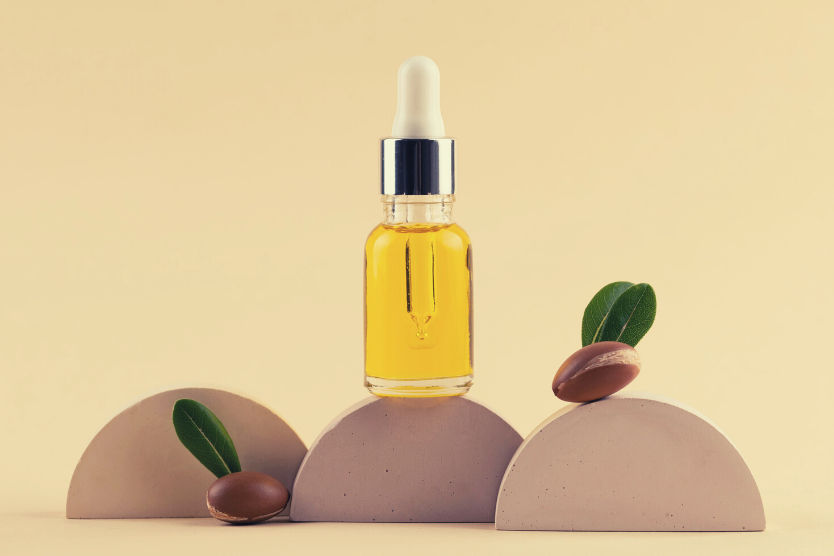 olejek-arganowy-w-butelce-z-pipetka-trzy-polkola-owoce-arganu-na-jasnobezowym-tle