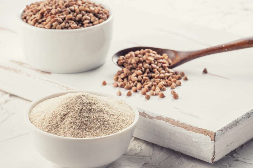 ziarna-kaszy-gryczanej-na-drewnianej-lyzce-kasza-gryczana-w-bialej-misce-maka-gryczana-w-bialej-misce-na-jasnym-tle