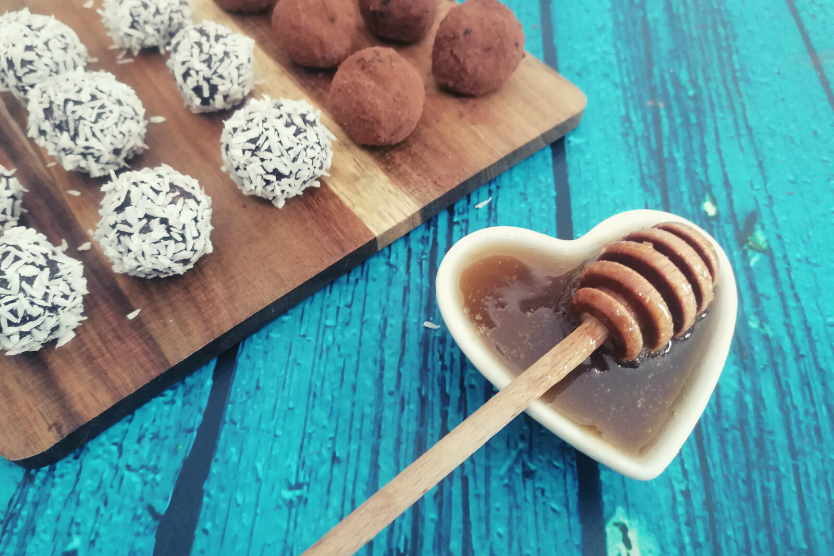 kulki-mocy-z-miodem-kuleczki-kokosowe-kuleczki-kakaowe-na-drewnianej-desce-bialy-pojemnik-z-miodem-na-niebieskim-tle