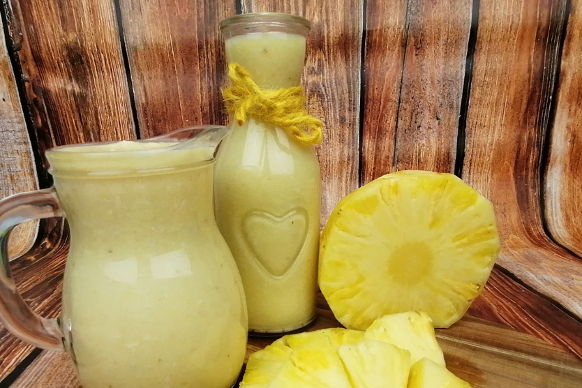 smoothie-z-bananem-ananasem-mleczkiem-kokosowym-wiorkami-kokosowymi-smoothie-w-szklanej-butelce-z-sercem-i-zoltym-sznurkiem-smoothie-w-malym-szklanym-dzbanuszku-ananas-przekrojony-na-pol-drewniane-tlo