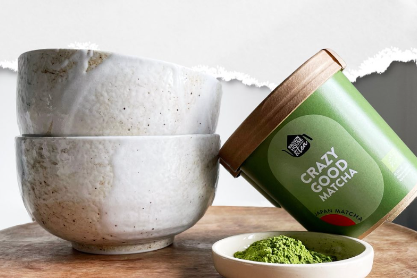 crazy-good-matcha-japan-organic-brown-house-tea-in-eco-friendly-packaging-displayed-on-a-wooden-surface-with-natural-ceramic-bowls-and-a-small-plate-of-green-matcha-powder-